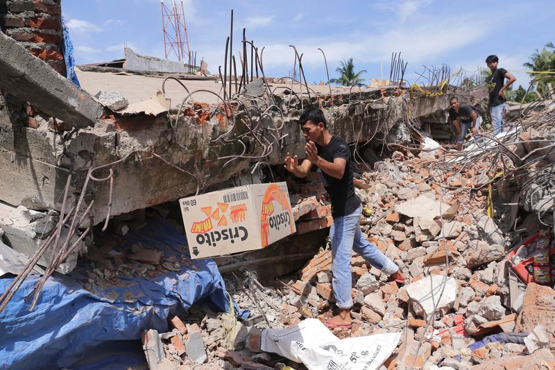 A man removes a box of food from under the rubble of a building that collapsed after the earthquake. (Image: AP/Heri Juanda)
